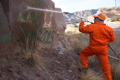 Operarios con hidrolavadoras trabajan esta tarde en la limpieza de los nombres que dejaron estampados con pintura en aerosol al menos tres turistas del conurbano bonaerense en rocas del Dique Potrerillos