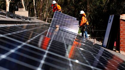 Operarios instalan paneles de energía solar en el techo de una casa en California