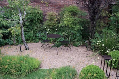 Orientado al sur y rodeado de medianeras, en este jardín no crecía césped, por eso, se op´to por delimitar la superficie con ladrillos de canto y cubrir con piedrita suelta el suelo para lograr un ambiente de uso bajo la sombra. Paisajismo: Eugenia Anaya.