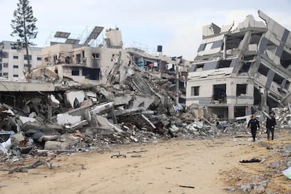 Palestinos caminan junto a un edificio destruido en el bombardeo israelí de la Franja de Gaza, en Ciudad de Gaza, el miércoles 3 de enero de 2024.