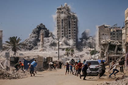 Palestinos corren a cubrirse durante un ataque israelí contra un edificio alto en Ciudad de Gaza, el viernes 5 de septiembre de 2025, después de que el Ejército israelí emitiera una advertencia