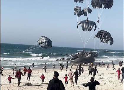 Palestinos corriendo hacia los paquetes con ayuda humanitaria lanzados desde aviones hacia la Franja de Gaza, el 2 de marzo de 2024 (Aline MANOUKIAN / AFP)