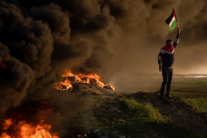 Palestinos queman neumáticos y ondean la bandera nacional durante una protesta contra una incursión militar israelí en la ciudad cisjordana de Yenín, junto a la valla fronteriza con Israel, en el este de la ciudad de Gaza, el jueves 26 de enero de 2023. Durante la incursión en la ciudad cisjordana de Yenín, las fuerzas israelíes mataron al menos a nueve palestinos, entre ellos una mujer de 60 años, e hirieron a varios más, según informaron las autoridades sanitarias palestinas, en uno de los días de enfrentamientos más mortíferos de los últimos años. El ejército israelí dijo que estaba llevando a cabo una operación para detener a militantes cuando estalló un tiroteo. (AP Photo/Fatima Shbair)