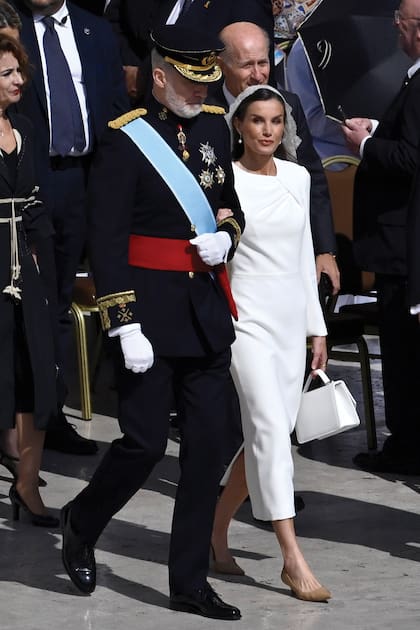 Para asistir a la misa inaugural de León XIV, Letizia eligió un vestido midi con escote asimétrico, de Redondo Brand, la firma del español Jorge Redondo. Llevó, además, pendientes de perlas, mantilla (era de la casa sevillana Lina; la última vez que Letizia usó mantilla fue en 2004, cuando se casó con Felipe) y cartera. Además del fajín rojo, el Rey lució su uniforme de capitán general del Ejército de Tierra con el Toisón de Oro, la banda de la Orden de Carlos III y otras condecoraciones.