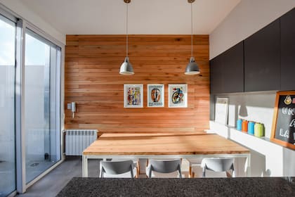 Para compensar del acero, en el comedor revisitó una pared a modo de deck vertical. Mesa con base de hierro pintada de blanco y tapa de paraíso (Estudio MPB) con ruedas, cómoda para llevar al patio. En el mueble de la cabecera, de 15cm de profundidad, guarda frascos y alimentos.