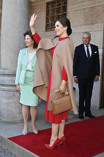 Para despedirse de los Bernadotte, Mary (en la foto junto a la reina Silvia durante la visita al museo Príncipe Eugens Waldemarsudde) optó por un vestido midi en color rojo de la diseñadora brasileña Raquel Diniz que había estrenado en 2017. Lo complementó con stilettos al tono Gianvito Rossi, abrigo tipo capa de pelo de camello y lana Oscar de la Renta, cartera y guantes color camel.
