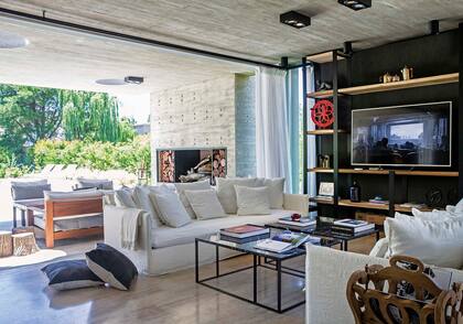 Rotunda biblioteca de hierro con estantes de madera de laurel y tiras de led embutidas (Estudio Pirca). Mesas bajas con tapas de mármol negro Marquina y sillones ´Gervasoni´ con fundas en lino