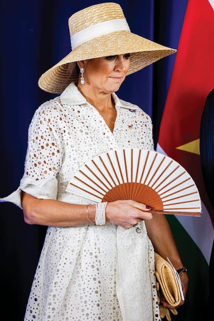 Para la ceremonia de bienvenida, la Reina volvió a elegir
a Natan, esta vez con un estreno: un vestido calado y cruzado de puños anchos y lazo en la cintura,
rematado por un broche de perlas y diamantes. Los accesorios –pendientes, anillo y brazalete de
varias vueltas– también son de perlas. Completó el look con una gran pamela de rafia