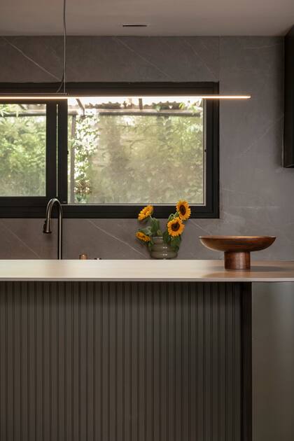 Para la isla se usó MDF varillado laqueado con mesada de Neolith y luminaria central que acompaña la iluminación de los spots empotrables (Boutique de Luz).