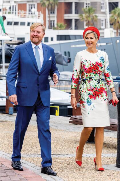 Para la visita al muelle de  Ciudad del Cabo, Máxima recuperó uno de sus vestidos más primaverales, un diseño de Natan de silueta recta, estampado con flores rojas sobre un fondo blanco. Y lo coordinó con los demás componentes de su estilismo: turbante de Fabienne Delvigne, zapatos de Natan y guantes cortos, todo en rojo. 