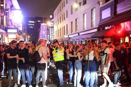 Un oficial de policía intenta decirle a los juerguistas que la calle se reabrió al tráfico de autos