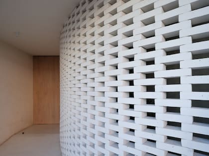 Para resguardar el ventanal del frente pero a la vez permitir el paso de luz, crearon un muro con una rejilla de ladrillos pintados de blanco. La puerta es de petiribí y el piso es de microcemento blanco.