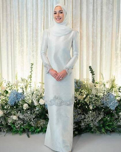 Para su primera aparición de blanco la novia deslumbró con un hiyab semitransparente que completó con un baju kurung hecho a medida con detalles bordados, encaje y acabados metalizados, diseñado por la firma Teh Firdaus, y el fabuloso anillo de compromiso con un diamante de gran tamaño.