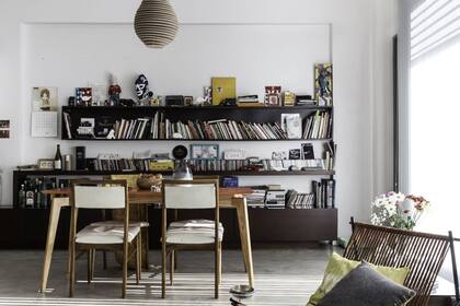Para sumarle color a este espacio se pintó la tapa de la mesa con un naranja intenso. El juego de sillas vintage está tapizado en cuero color natural. Detrás, una gran biblioteca hecha a medida sirve como espacio de guardado y marco al espacio