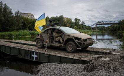Paracaidistas ucranianos cruzan un puente militar sobre el río Siverskiy-Donets en un auto con una bandera ucraniana, en Izium, una zona ucraniana recién recuperada a las tropas rusas, el 14 de septiembre de 2022. (AP Foto/Evgeniy Maloletka)