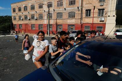 Los niños buscan comida entregada por una mujer en un automóvil que pasa en el barrio pobre de Chacarita en Asunción