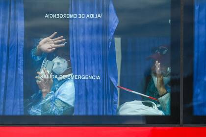 Pasajeros evacuados del crucero MV Hondius saludan desde un autobús militar tras ser trasladados al puerto de Granadilla de Abona, en Tenerife, el 10 de mayo de 2026
(Photo by JORGE GUERRERO / AFP)