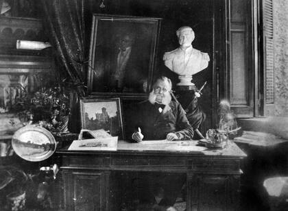 Pastor Obligado retratado en su escritorio, a su lado una pintura de su residencia sobre Avenida Alvear, circa 1886.