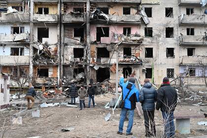 Un grupo de personas observa un edificio residencial dañado en la calle Koshytsa, suburbio de la capital ucraniana, Kiev, donde supuestamente cayó un proyectil militar, el 25 de febrero de 2022. (Foto de GENYA SAVILOV / AFP)