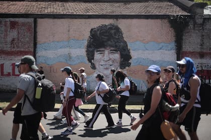 Peregrinos pasan frente a un mural con la imagen de Diego Maradona