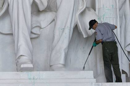 Personal de limpieza intenta quitar la pintura verde del pedestal y una pierna de la escultura