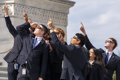 Personal del Senado utiliza gafas para eclipses mientras ven la luna cubriendo parcialmente al sol durante un eclipse solar total, frente al Senado de Estados Unidos en el Capitolio, el lunes 8 de abril de 2024, en Washington