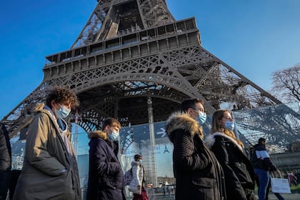 Personas con mascarillas para protegerse del COVID-19 caminan frente a la Torre Eiffel, el martes 21 de diciembre de 2021, en París. (AP Foto/Michel Euler)