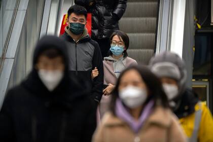 Personas con mascarillas suben por una escalera mecánica en un complejo comercial y de oficinas en Pekín