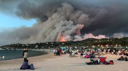 Personas evacuadas encontraron refugio en la playa y miran un incendio quemando el bosque en Bormes-les-Mimosas, al amanecer en el sur de Francia