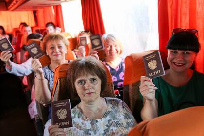 Personas muestran sus pasaportes rusos mientras se sientan en un autobús para viajar a Rusia para votar sobre las enmiendas constitucionales en la vecina región de Rostov en Rusia, en una parada de autobús en Donetsk, una región controlada por los separatistas en el este de Ucrania, el 27 de junio de 2020. 