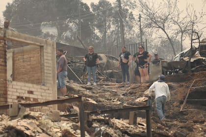 Personas observan los escombros de casas destruidas por un incendio forestal, en Viña del Mar, Chile