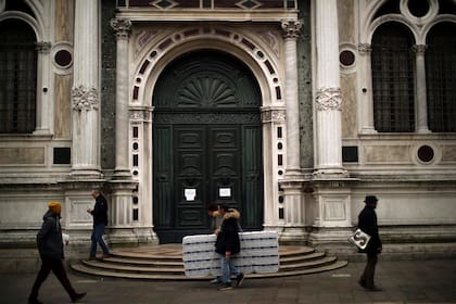 Personas pasan frente a la iglesia de St Roch, cerrada temporalmente debido al brote del virus COVID-19, en Venecia, el sábado 29 de febrero de 2020.