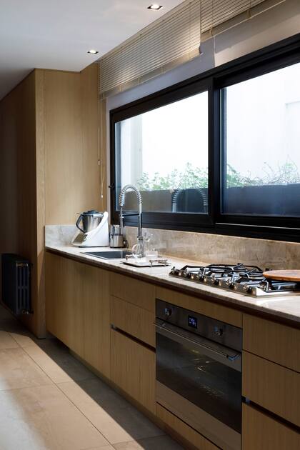 Piso de Travertino (SBG), amoblamiento de cocina en roble americano (De Otro Tiempo) con mesada de cuarcita ‘Taj Majal’ (De Stefano) y bacha (Mi Pileta).