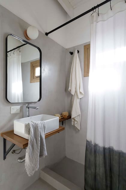 Piso y revestimiento de cemento alisado (Miracema). Mesada de madera con bacha de apoyo (Rocca) y grifería (FV). Espejo (Za Mobiliario Industrial), lámpara (Dimm) y cortina de baño (Maru Bardó).