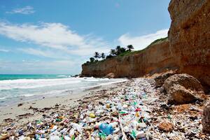 Plastic trash on the sea sandy white beach. Rocky coast of the peninsula in the ocean. Sea waves on a sunny day.
