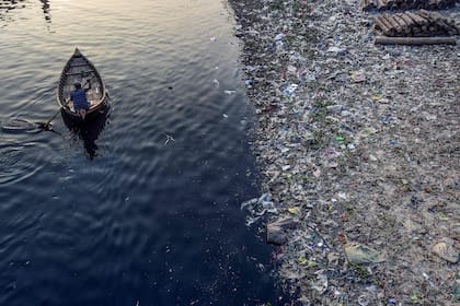 Un hombre rema en un bote mientras bolsas de plástico flotan en la superficie del agua del río Buriganga en Dhaka.