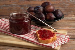 Plum confiture in a glass jar with toast breads and fruits on a kitchen towel