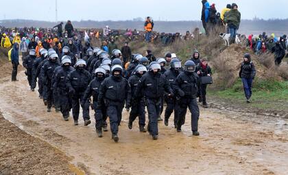 Police officers walk next to people who attend a protest rally at the Garzweiler opencast mining near the village Luetzerath in Erkelenz, Germany, Saturday, Jan. 14, 2023. Swedish climate campaigner Greta Thunberg takes part in that protest rally after she visited the tiny village of Luetzerath on Friday and took a look at the nearby Garzweiler open coal mine. (AP Photo/Michael Probst)