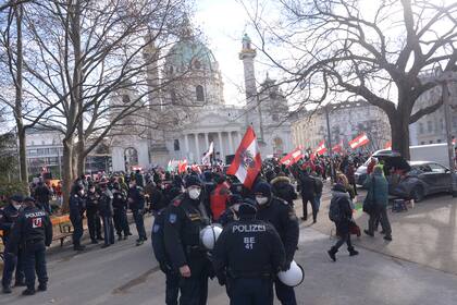 Policías junto a manifestantes sosteniendo banderas austriacas durante una protesta contra las restricciones y medidas adoptadas por el gobierno de Austria para combatir el nuevo coronavirus, el 13 de febrero de 2021 en Viena