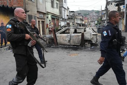 Policías pasan junto a un coche quemado que fue utilizado como barricada durante una operación policial contra presuntos narcotraficantes en la favela Complexo do Alemao, donde opera la organización criminal "Comando Vermelho", en Río de Janeiro