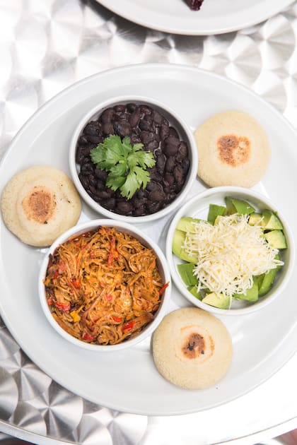 Porotos negros, carne desmechada, queso llanero, palta y arepas para un desayuno tardío.