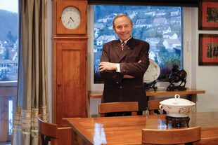 Posa en el comedor de su casa, que tiene grandes ventanales a través de los cuales se ve la aldea de montaña.