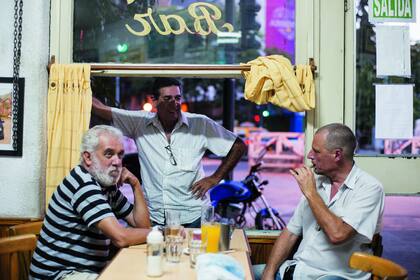 Postal diaria: Mario escucha a Rubén, que fuma su cigarrillo electrónico. El Turco participa de la charla desde afuera: cuando deje de fumar se sentará a la mesa