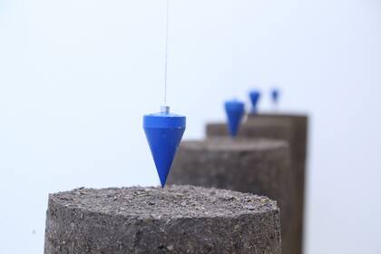 Instalación de tierra compactada en columnas con plomadas que indican el centro, de la tucumana Sofía Noble