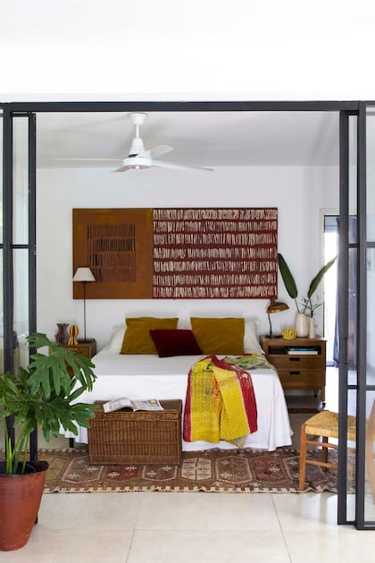 Puerta corrediza en hierro negro y vidrio, que separa el dormitorio de la sala sin perder luz. Sobre el respaldo, una obra que Ángeles pintó en un bastidor de madera que encontró dando vueltas en su taller. La alfombra era de su madre, que la trajo de Turquía hace años.