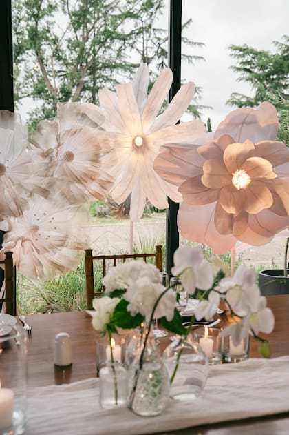 "Quisimos replicar la estética simple de las flores blancas sobre la mesa, llevándolas a una gran escala y diseñamos estas flores gigantes de papel con iluminación central para que se puedan apreciar también de noche", contó Lucila de esta ambientación de la mesa principal de un casamiento.