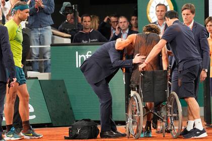 Rafael Nadal mira cómo Alexander Zverev se sienta en una silla de ruedas para abandonar una semifinal de Roland Garros en 2022; el alemán se rompió siete ligamentos por una torcedura de tobillo.