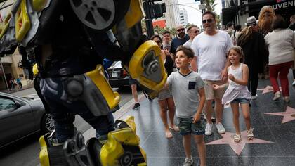 Ramiro Rodríguez en un traje Bumblebee, un personaje de la serie de películas Transformers, estrecha la mano con los jóvenes turistas en Hollywood Boulevard, en Los Ángeles.
