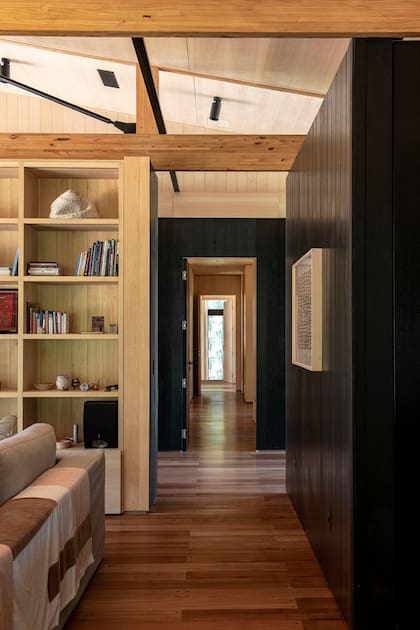 Realzadas por su contraste con el negro, las paredes del pasillo fugan hacia el extremo de la casa donde se ubican los dormitorios.