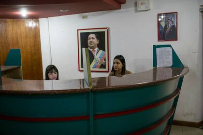 Recepcionistas trabajan cerca de retratos del difunto presidente de Venezuela, Hugo Chávez, en el centro, y del actual presidente, Nicolás Maduro, arriba a la derecha, dentro de una oficina administrativa en un mercado de alimentos en Caracas, Venezuela, el 28 de enero.